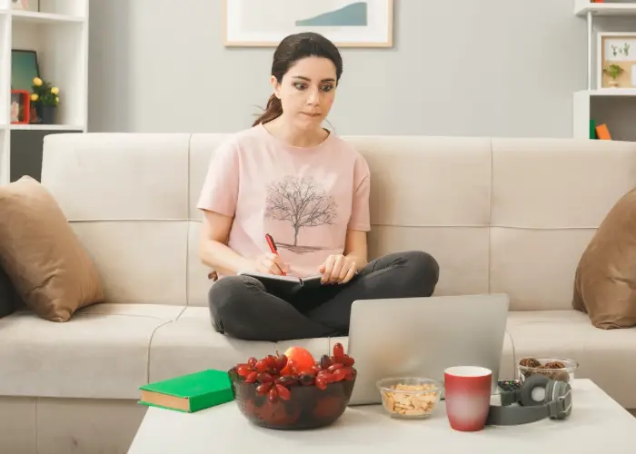 Woman taking notes in front of a laptop with a bowl of fresh fruit on the table, planning her thyroid management diet.