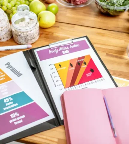Clipboard displaying a food pyramid and BMI chart next to a notebook, used for creating sustainable Women's Health & Wellness Nutrition Plans.